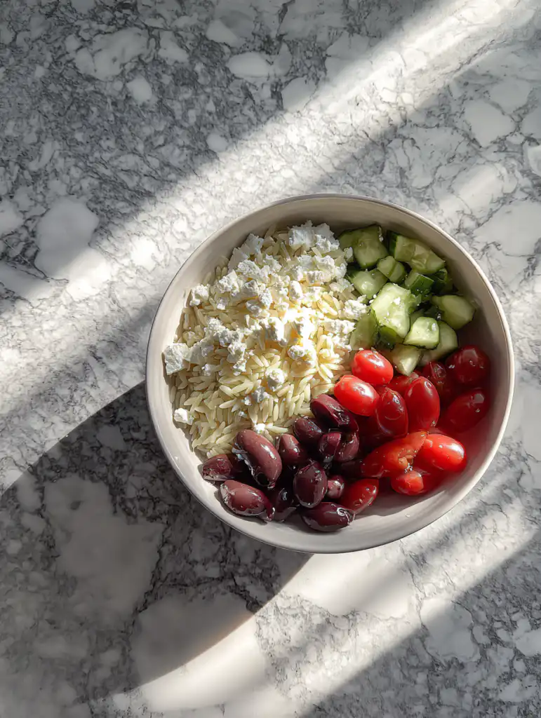 Greek orzo salad with feta preparation mixing orzo with vegetables and feta in bowl