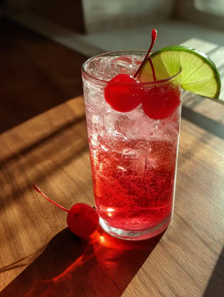 Shirley temple drink in a glass with cherry and lime garnish on wooden table