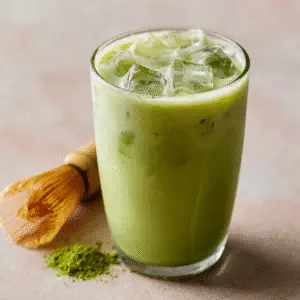Low Calorie Iced Matcha Latte served with ice cubes and a matcha whisk beside it